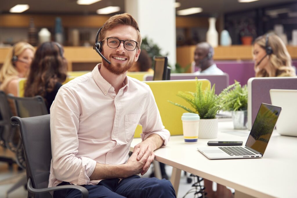 Portrait Of Businessman Wearing Headset Talking To Caller In Customer Services Centre